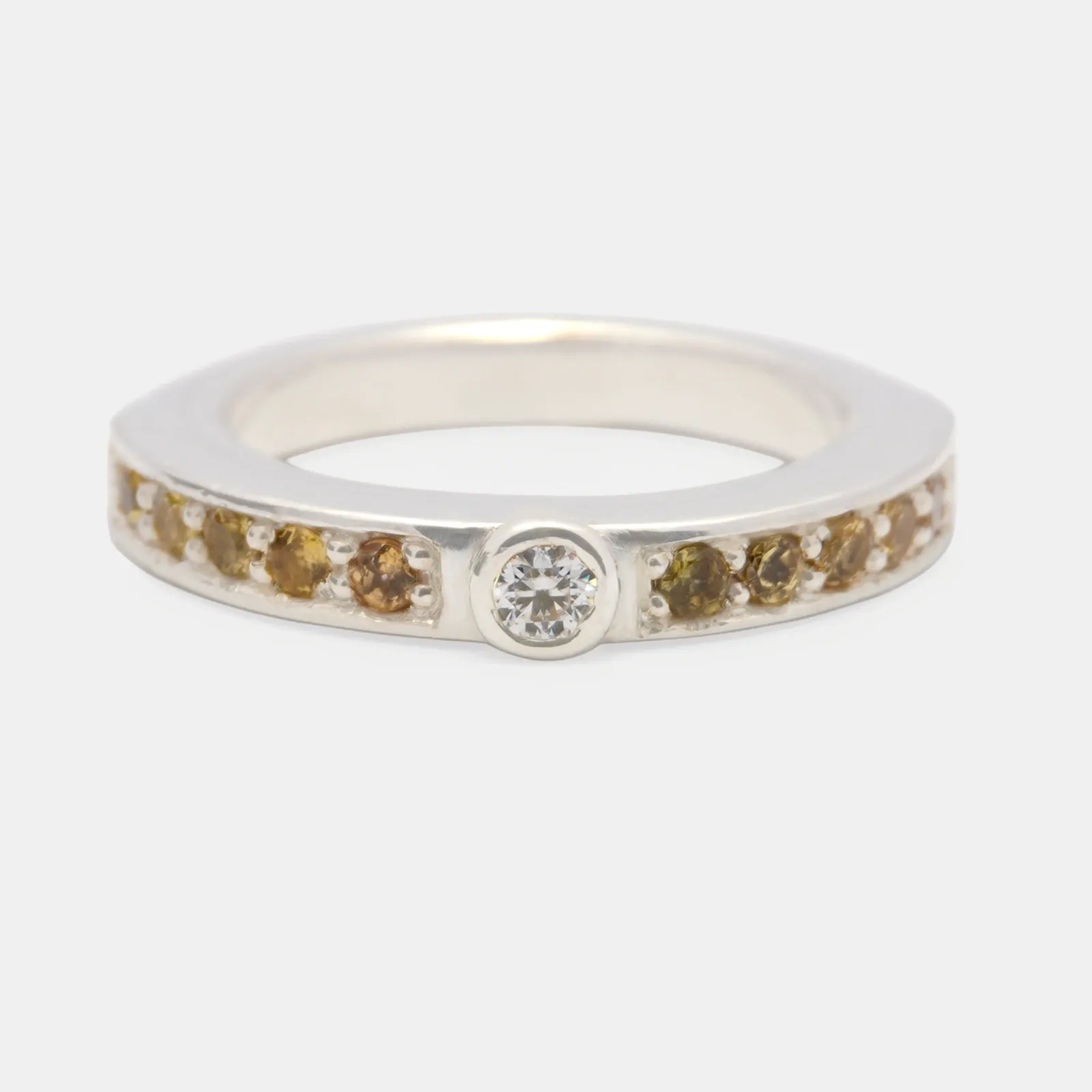 Anillo de plata de aro ancho, con una piedra blanca en bisel al centro y una hilera de granates de tono ámbar a cada lado.