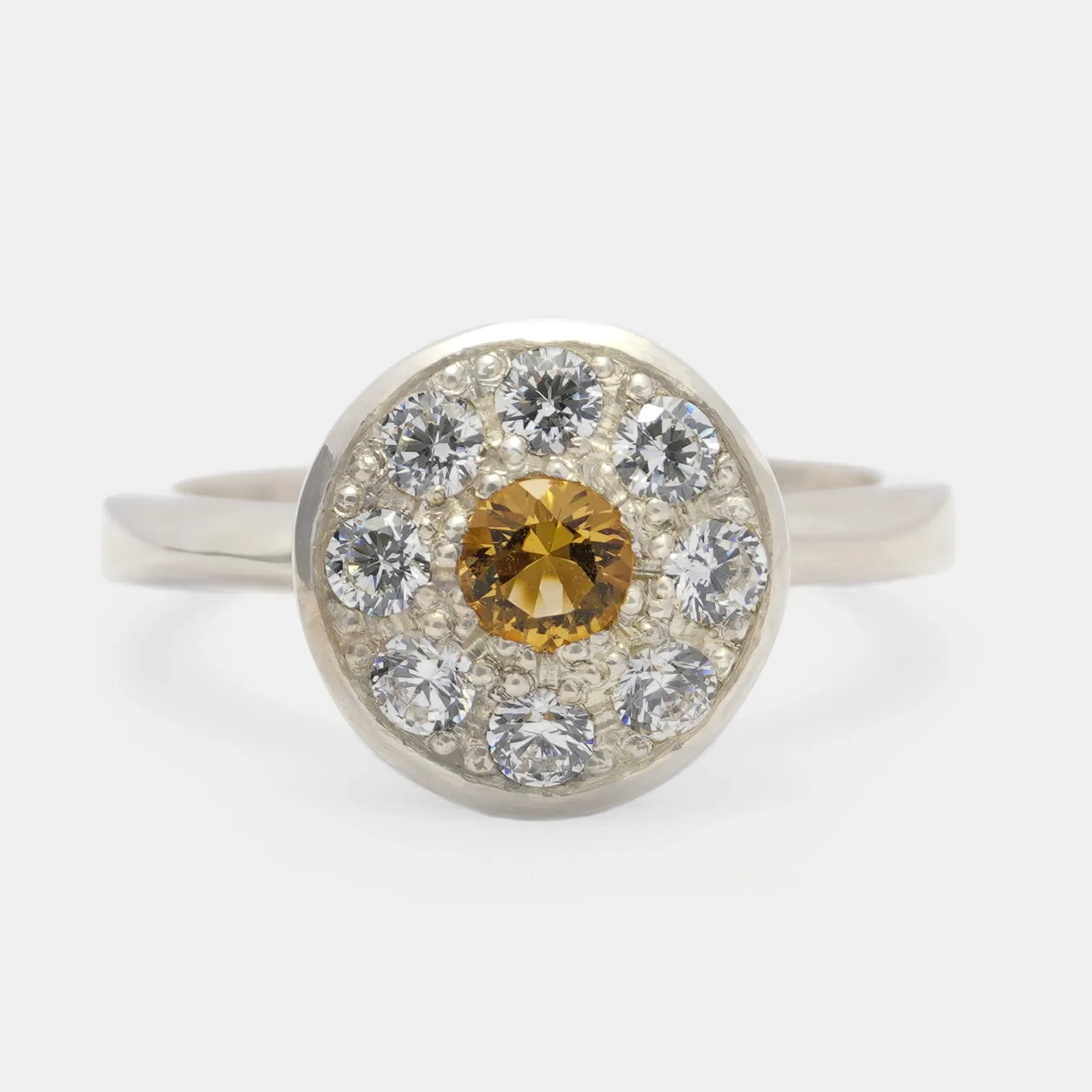 Anillo de plata visto de frente, con un citrino dorado al centro rodeado por un anillo de piedras blancas.