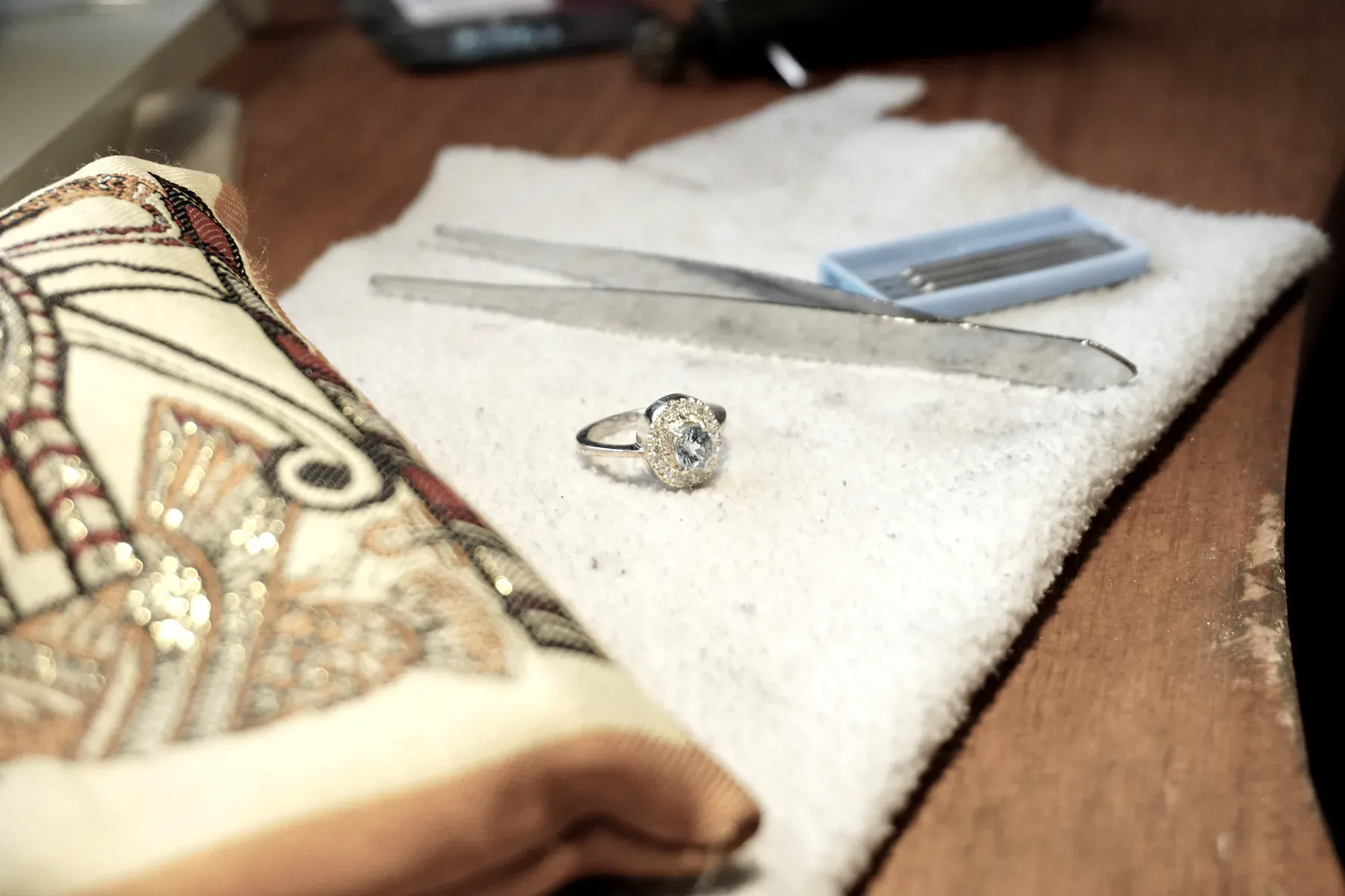 Un anillo terminado junto a pinzas y buriles sobre el paño del banco.